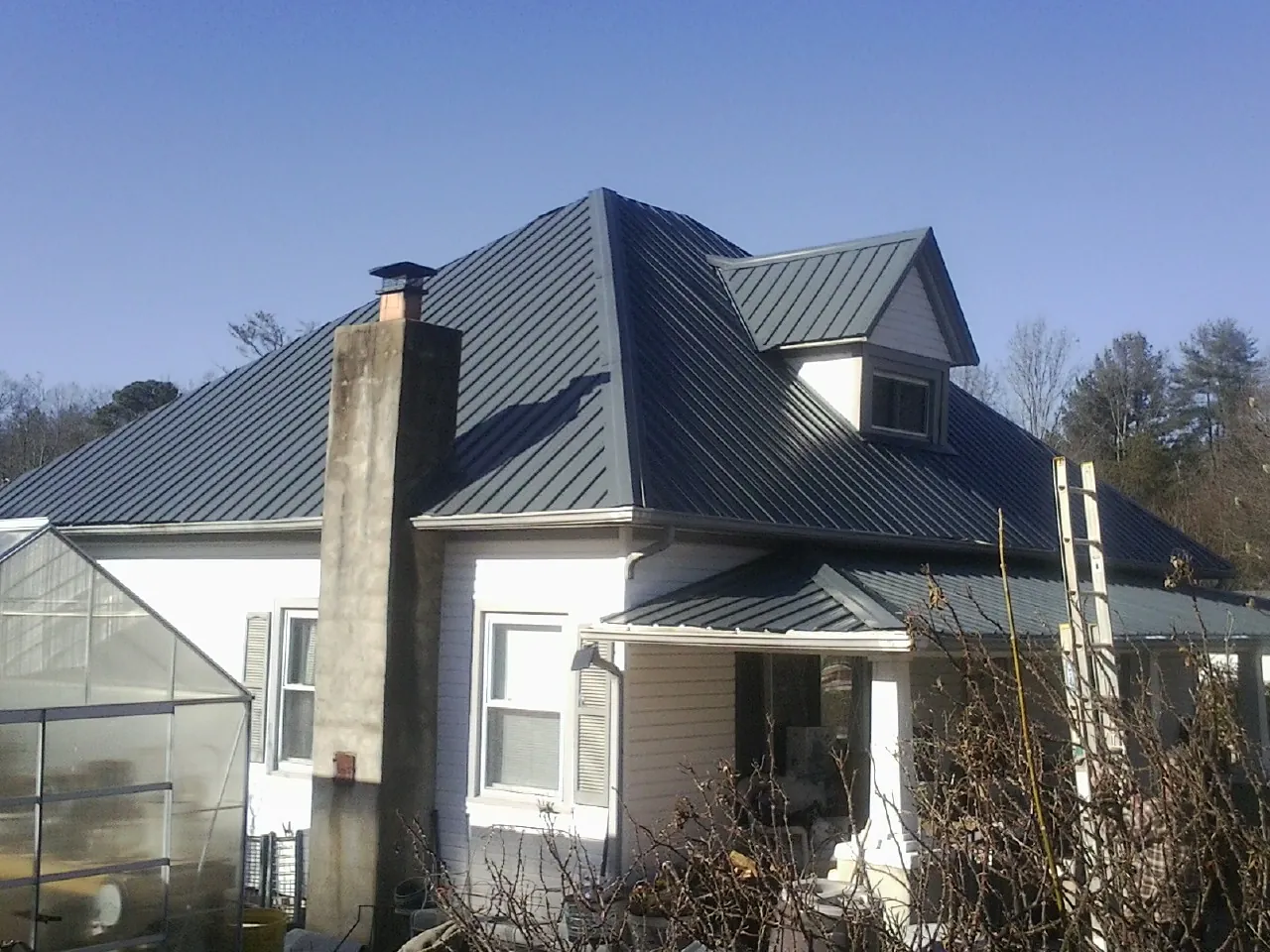 Dark blue standing seam metal roof on a white farmhouse with dormer — Slate & Tile Roof Repair by Roofing Brothers in Indio