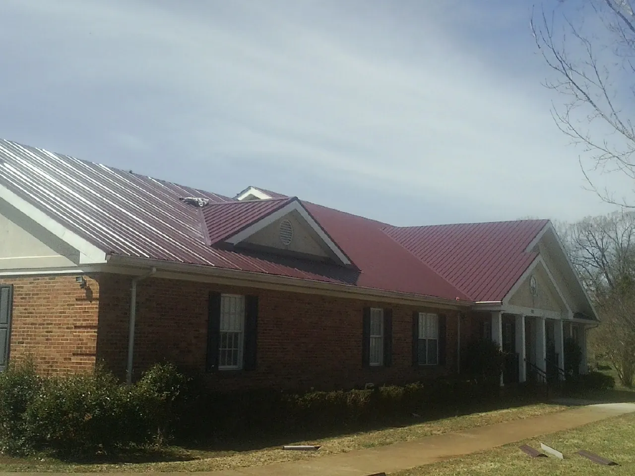 Red metal roof with gabled entries on a long brick building, from a Hail Damage Roof Repair job in Indio