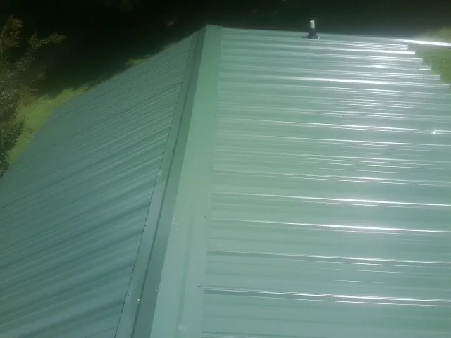 New green metal panels meeting at the ridge of a roof — Flat Roof Repair work by our crew in Indio