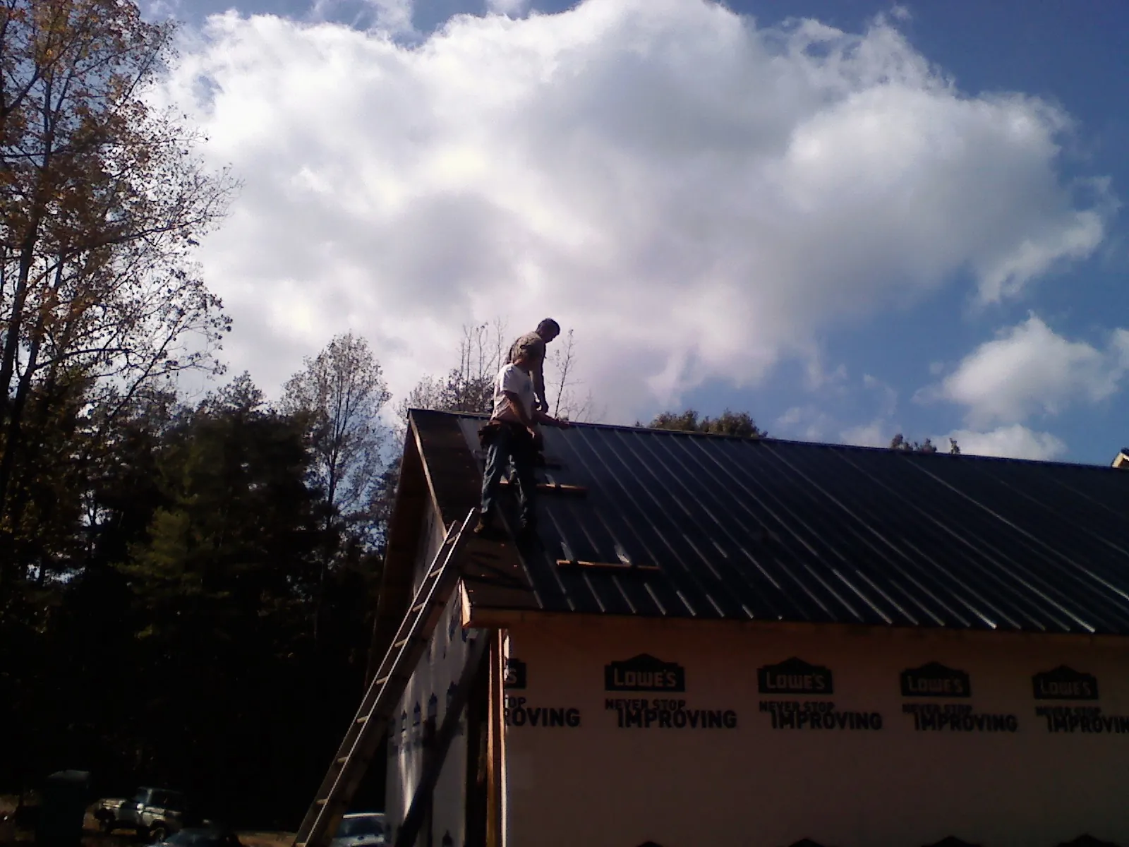 Roofer fastening dark metal panels high against a cloudy sky, from a Roof Inspection job in Indio