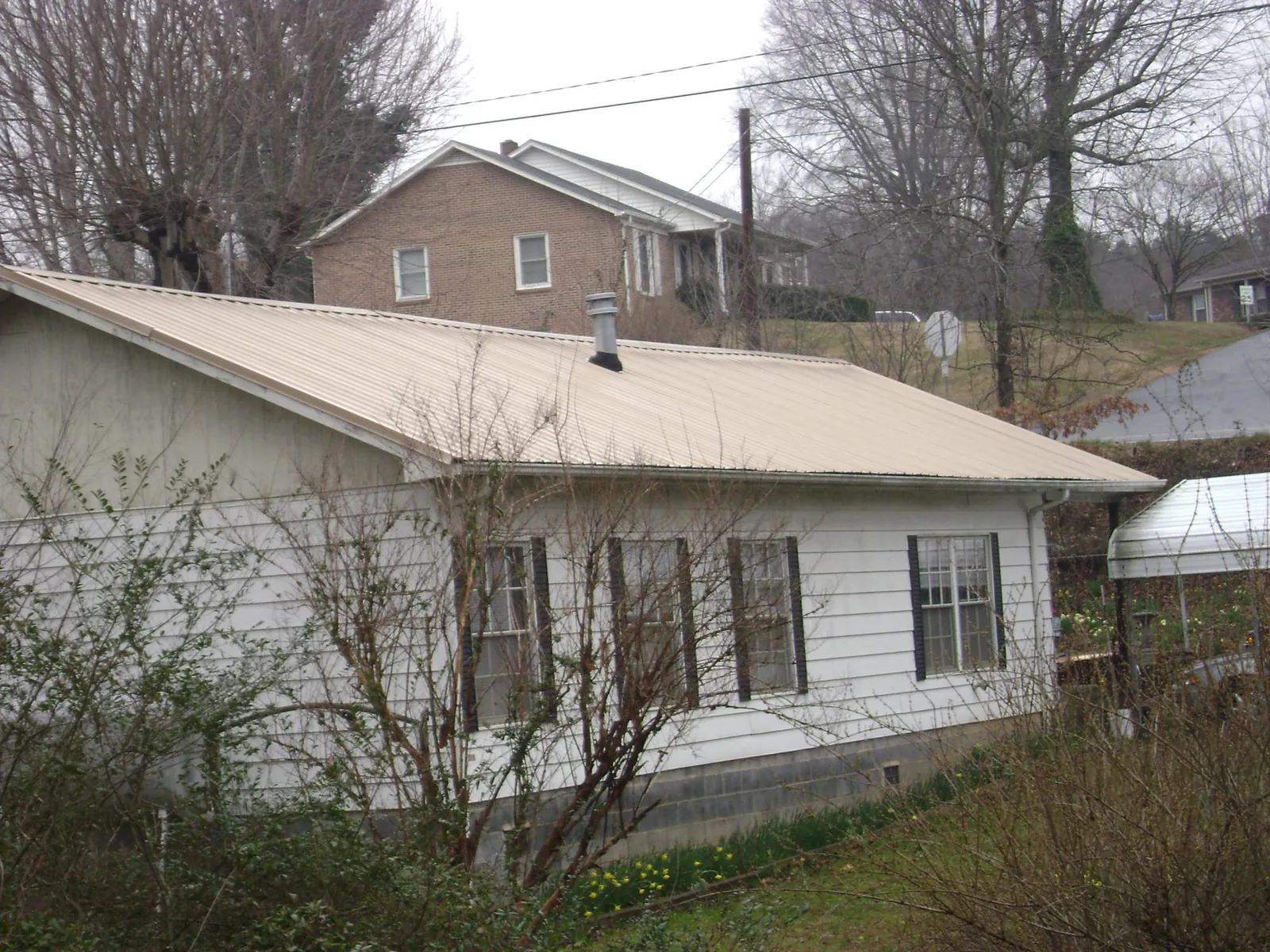 Tan metal roof on a white sided house set into a hillside — Commercial Roofing by Roofing Brothers in Indio